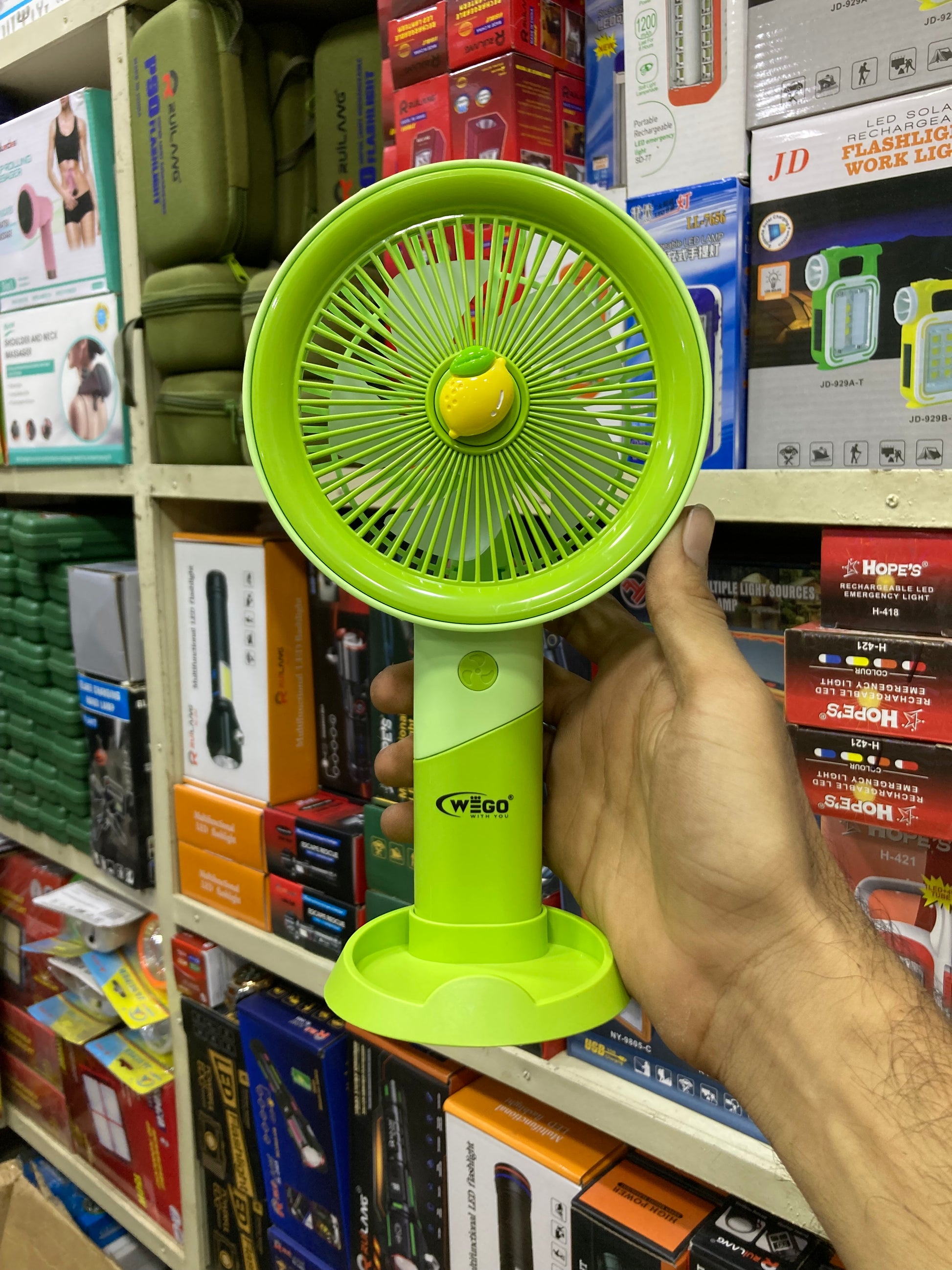 Green handheld fan held by a person in a store setting with various products in the background